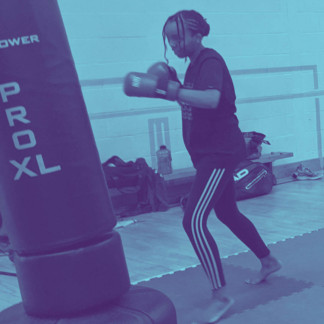 Blue tinted image of woman punching a punch bag.
